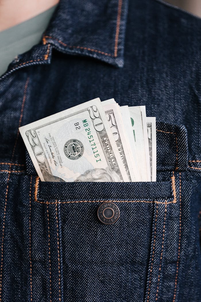 Close-up of US dollar bills in a denim jacket pocket, symbolizing wealth and finance.
